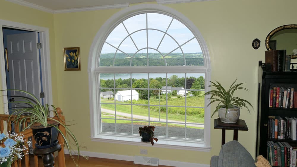 Large arched window with muntins overlooking lake and green hills