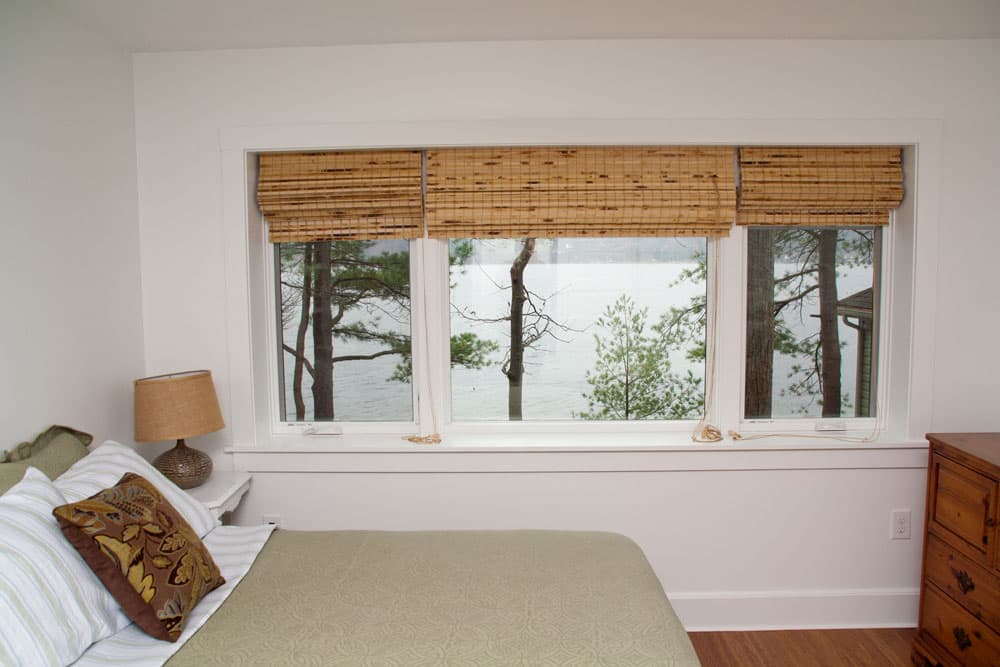 Bedroom with large window overlooking lake with bamboo shades and wooden dresser