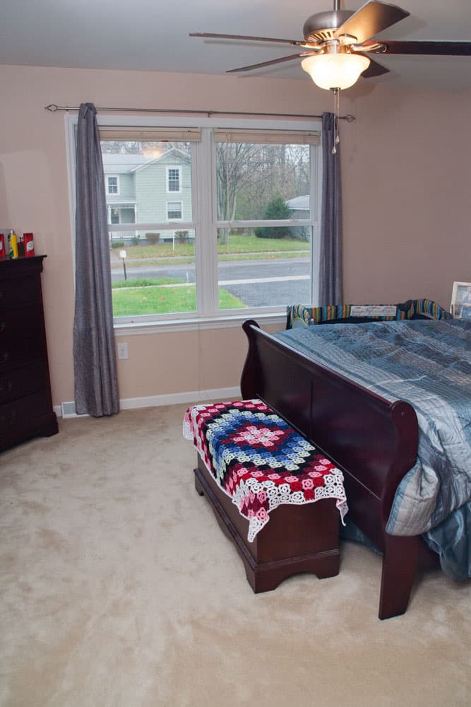 Bedroom with dark wood furniture, ceiling fan, and double windows overlooking street