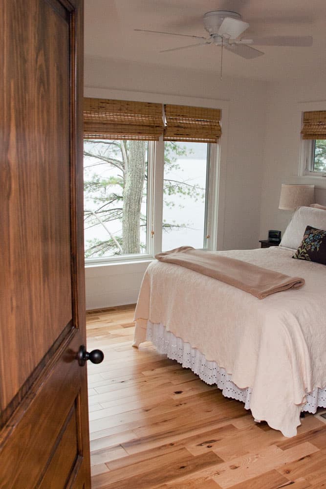 Bedroom with natural wood flooring, white bedding, and woven bamboo shades