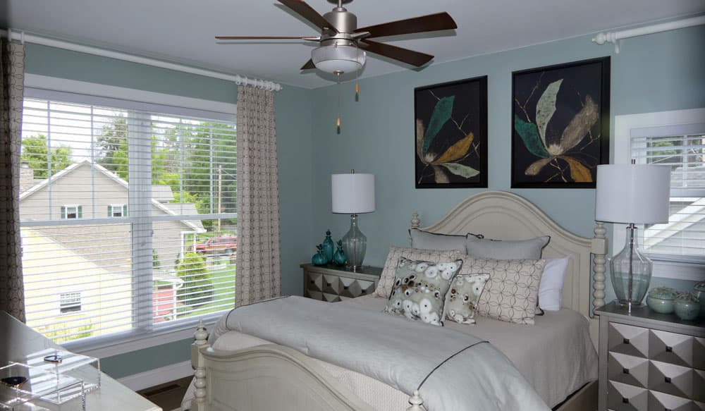 Bedroom with light blue walls, white bedding, botanical artwork, and two windows