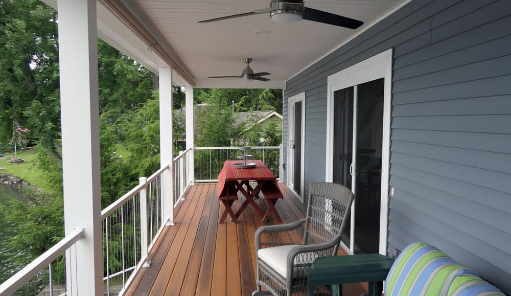 Covered second-story deck with wood flooring, ceiling fans, and white metal railings overlooking backyard