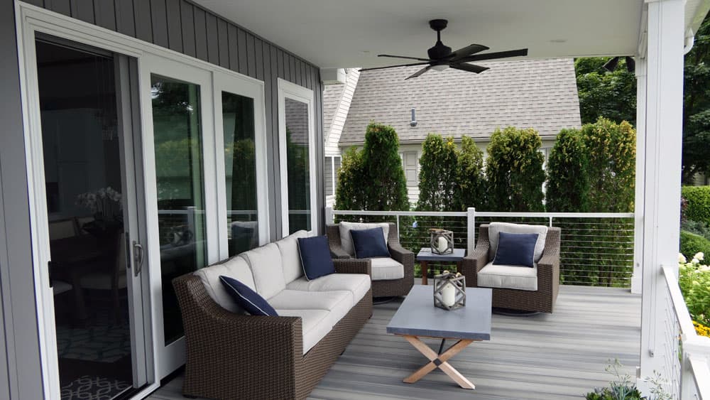 Covered deck with wicker furniture, ceiling fan, and cable railing overlooking yard