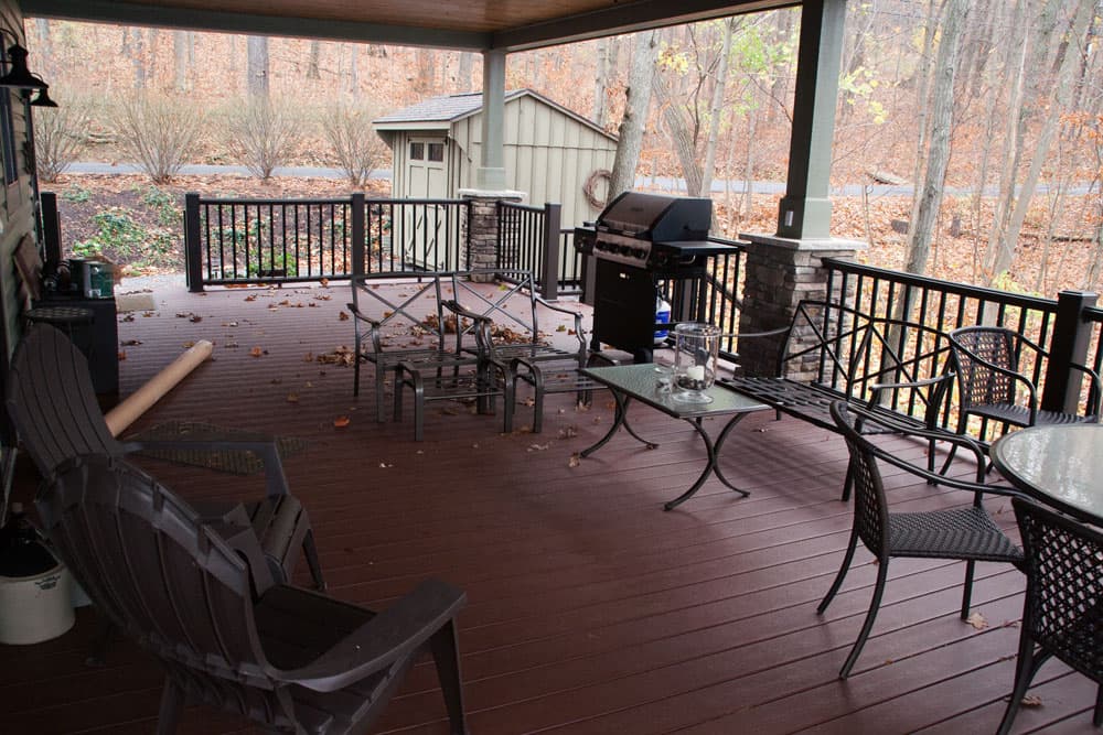 Covered deck with outdoor furniture and grill overlooking wooded lot in autumn