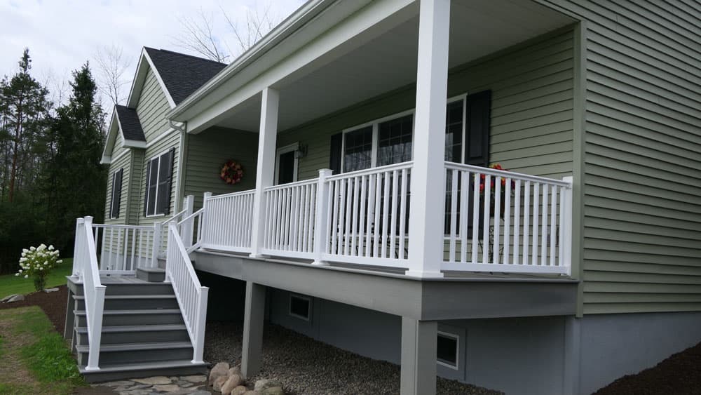 Covered front porch with white railings and stairs on green-sided house