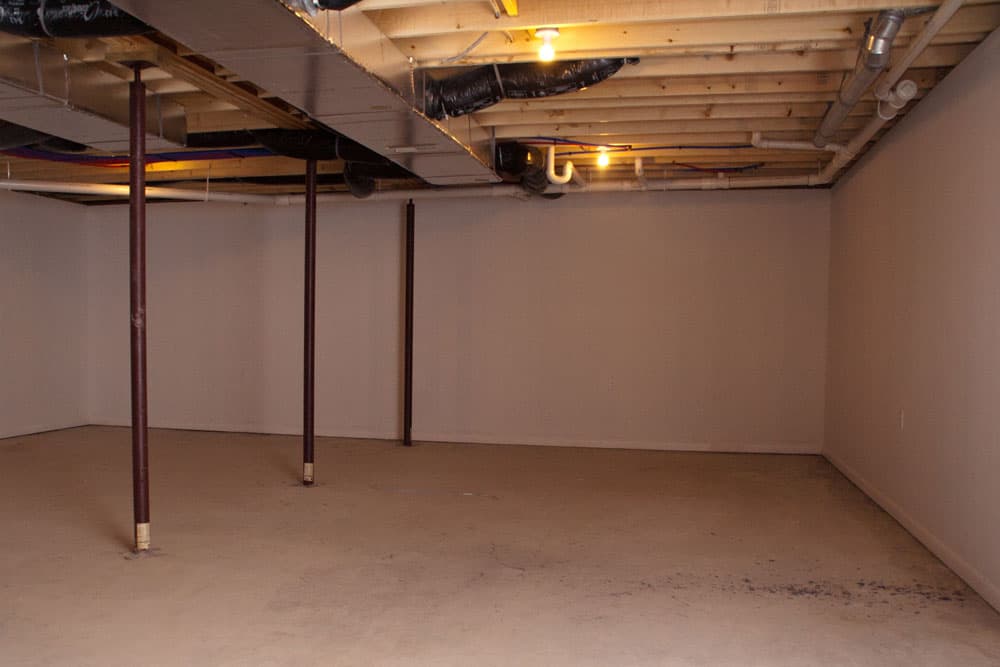 Empty basement with exposed ceiling joists, support posts, and concrete floor