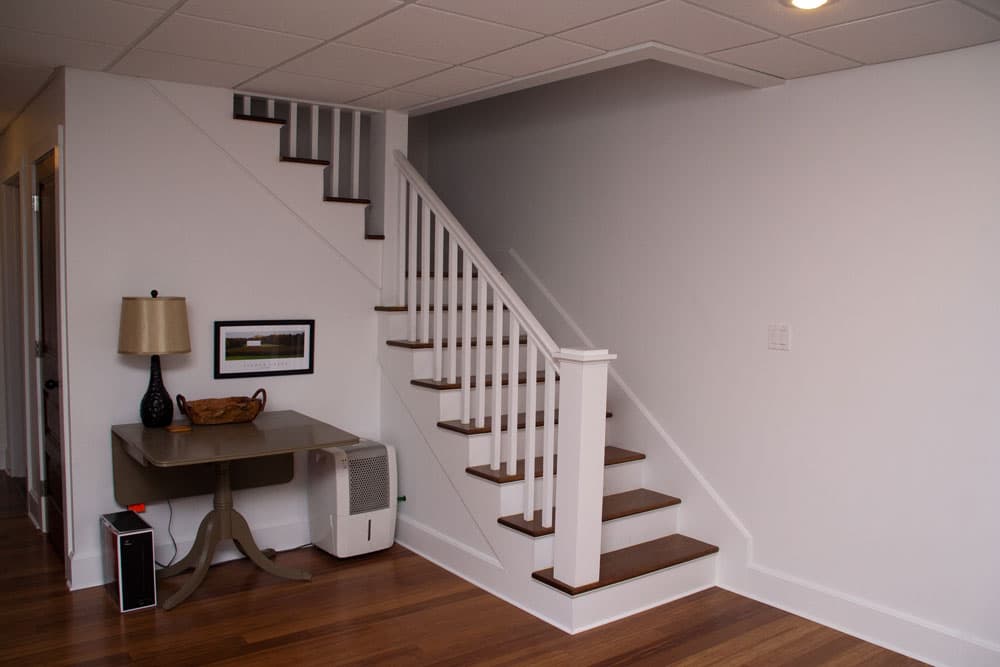Finished basement with white and wood staircase, drop ceiling, and hardwood flooring