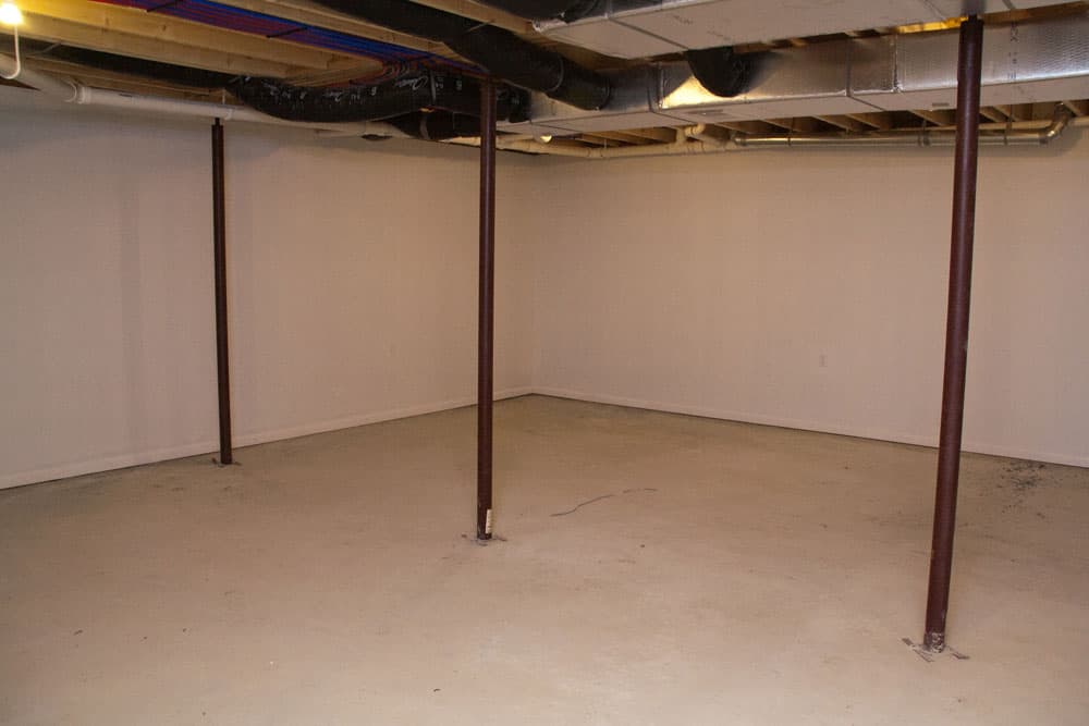 Empty basement with white painted walls, beige floor, and metal support columns