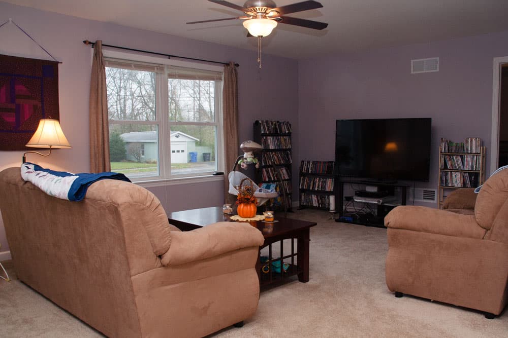 Living room with beige furniture, large TV, media storage, and ceiling fan