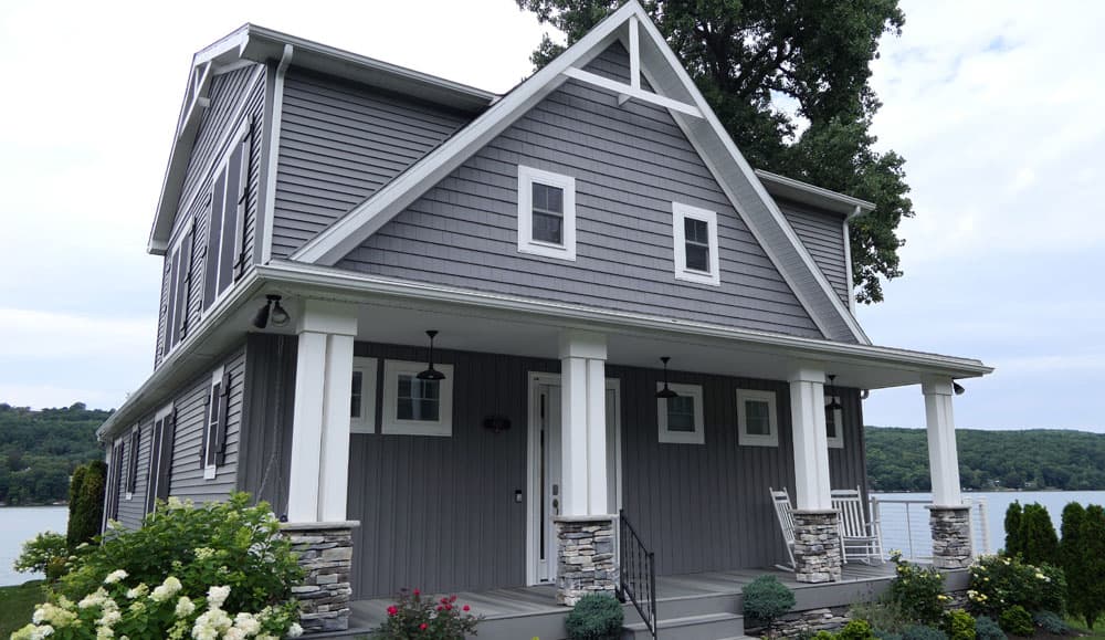 Gray modular home with white trim and covered porch overlooking lake