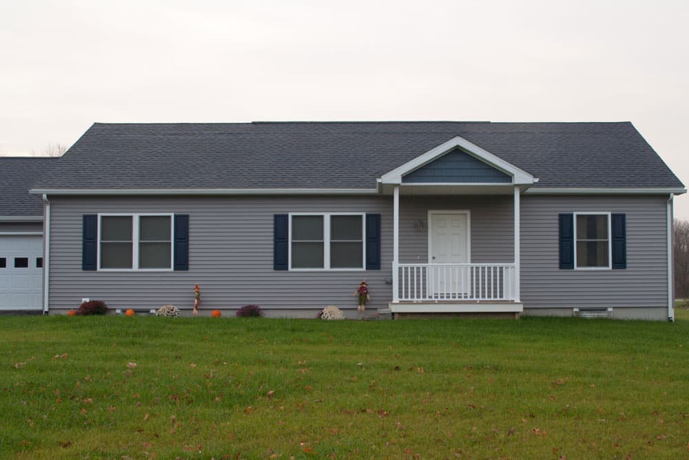 Gray ranch-style modular home with white trim, covered front porch, and black shutters