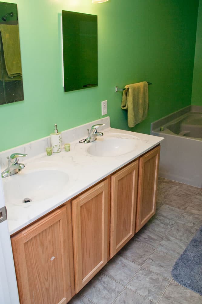 Bathroom with green walls, oak vanity, white countertop, and built-in bathtub