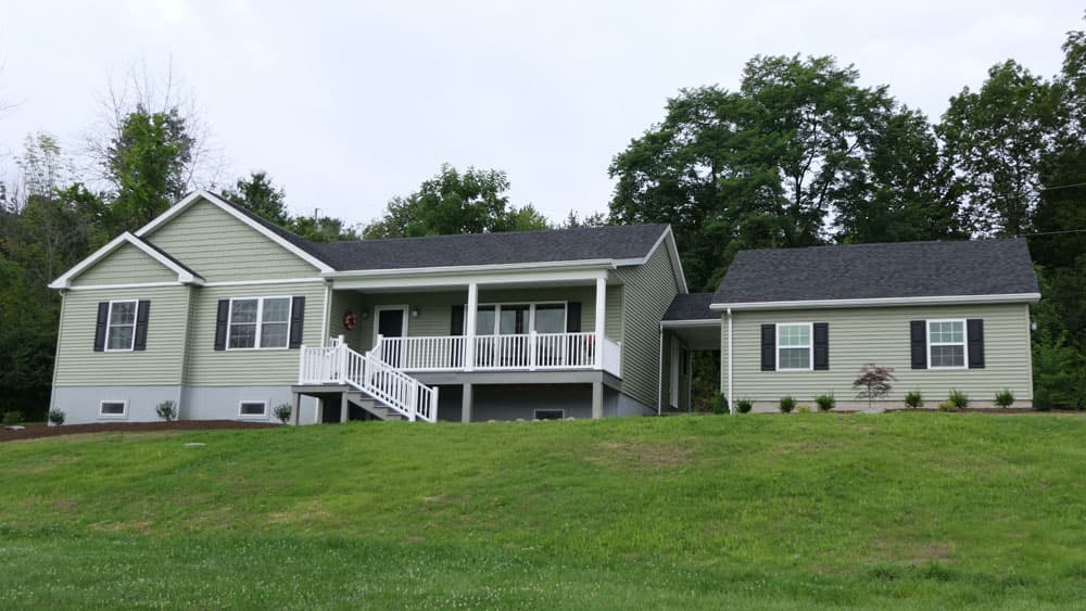 Green vinyl siding modular home with front porch and attached wing addition