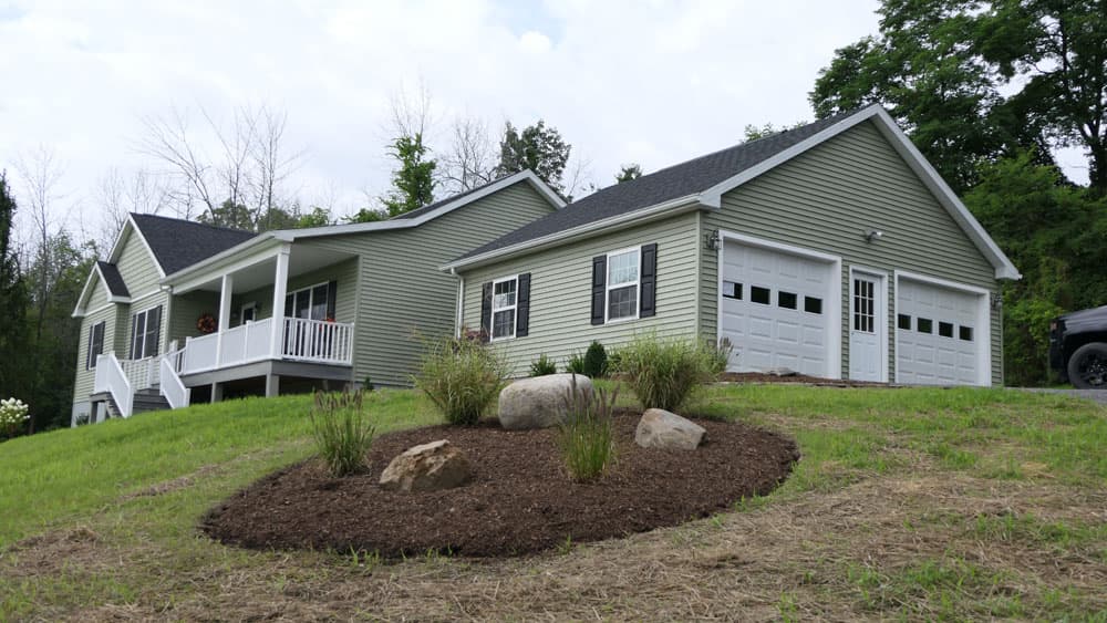 Green vinyl-sided modular home with covered porch and two-car garage