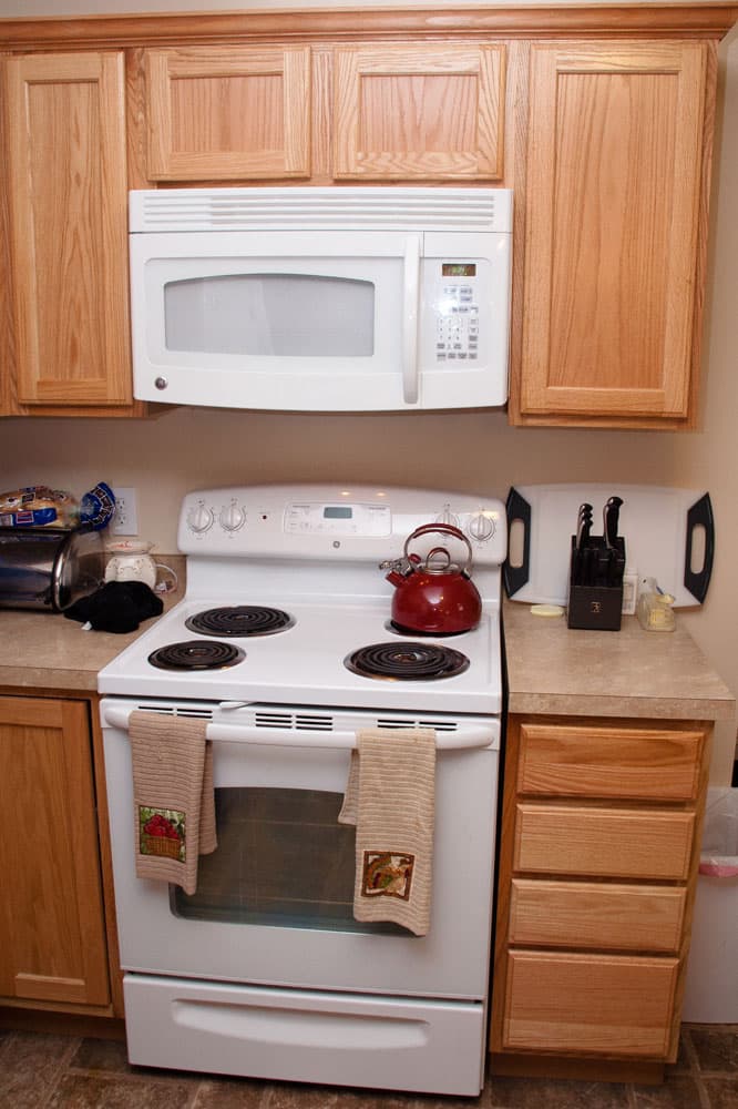 Kitchen featuring white electric stove with red kettle and oak cabinets