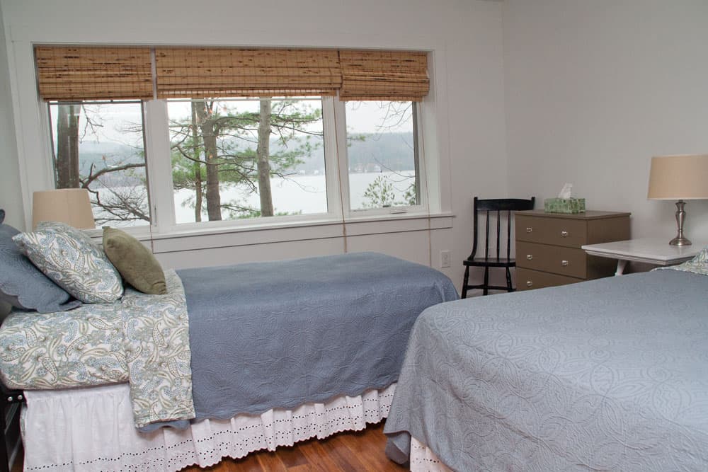 Bedroom with twin beds and bamboo shades overlooking lake and trees