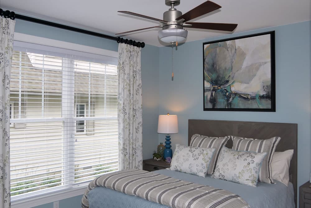 Bedroom with light blue walls, gray upholstered bed, and ceiling fan