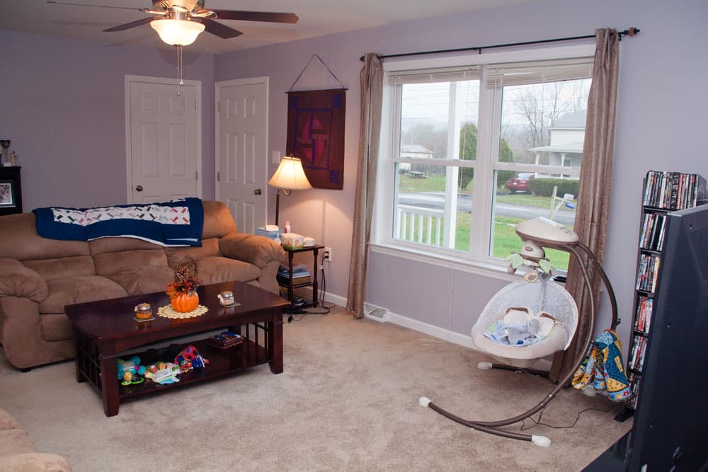 Living room with beige furniture, large window, and baby swing stand