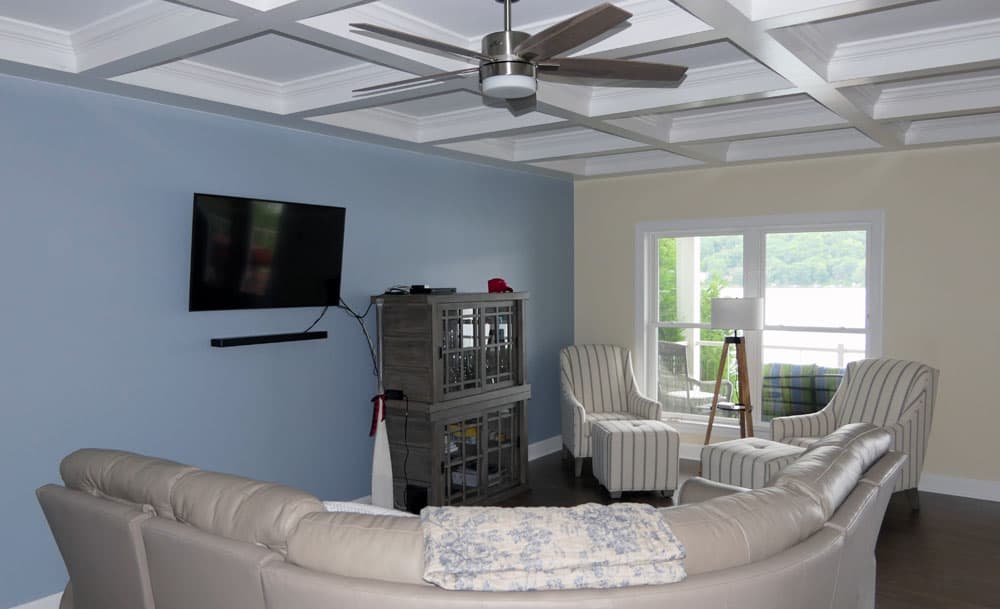 Living room with coffered ceiling, ceiling fan, beige sofa, and striped accent chairs