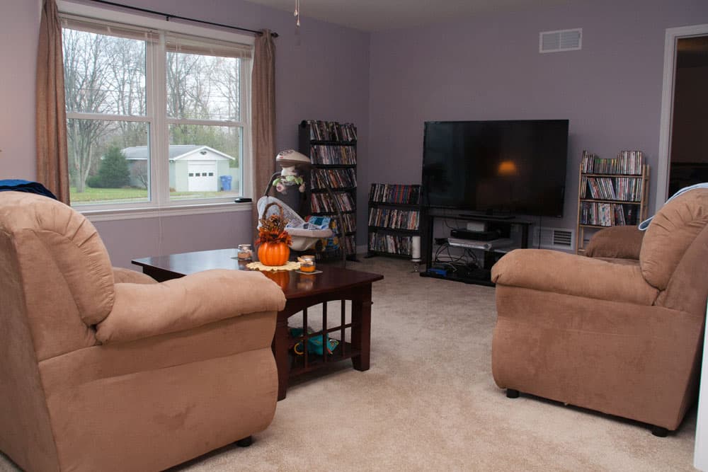 Living room with tan recliners, flat screen TV, and DVD collection shelves