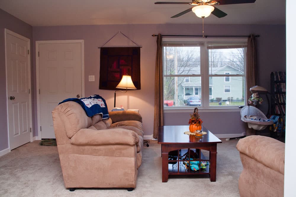 Living room with beige furniture, ceiling fan, and large windows overlooking neighborhood