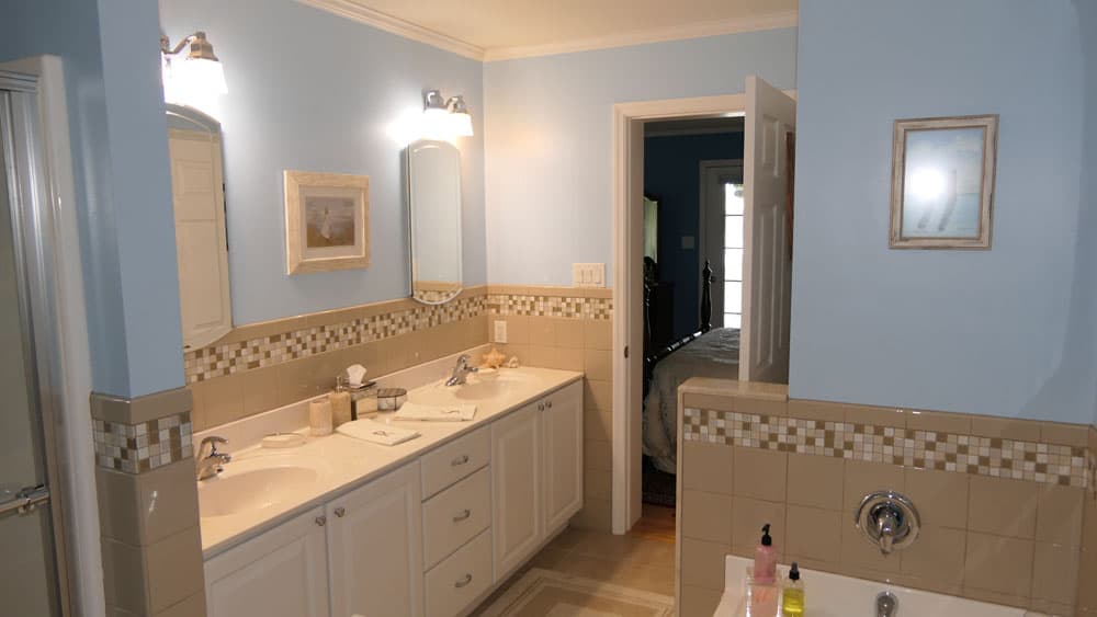 Master bathroom with blue walls, beige tile, dual vanity, and mosaic accent stripe