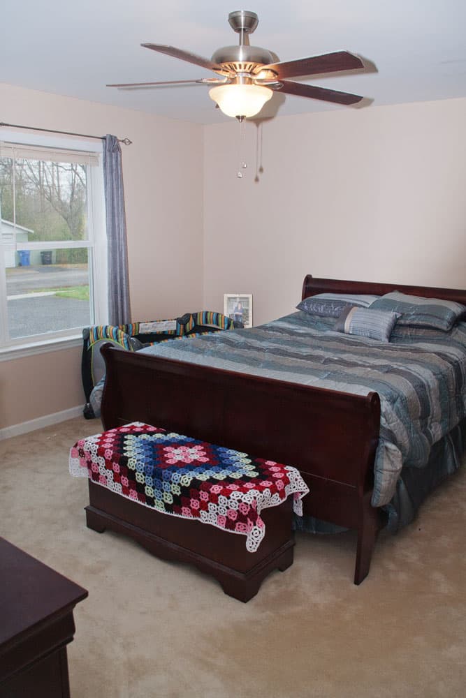Master bedroom with dark wood sleigh bed, ceiling fan, and window overlooking street