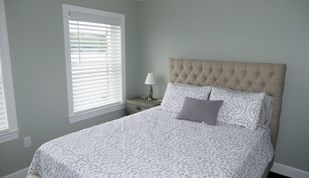 Bedroom with tufted beige headboard, patterned bedding, and pale blue walls