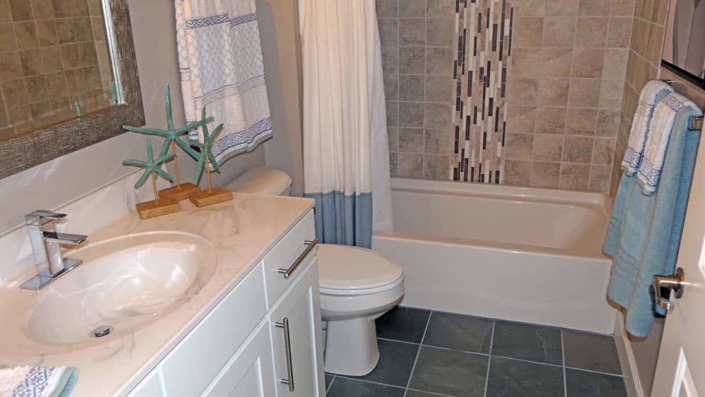 Renovated bathroom with beige tile walls, white vanity, and dark slate floor