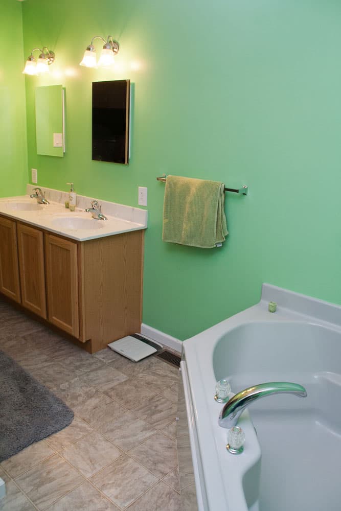 Bathroom with turquoise gradient walls, oak vanity, white countertop, and corner bathtub