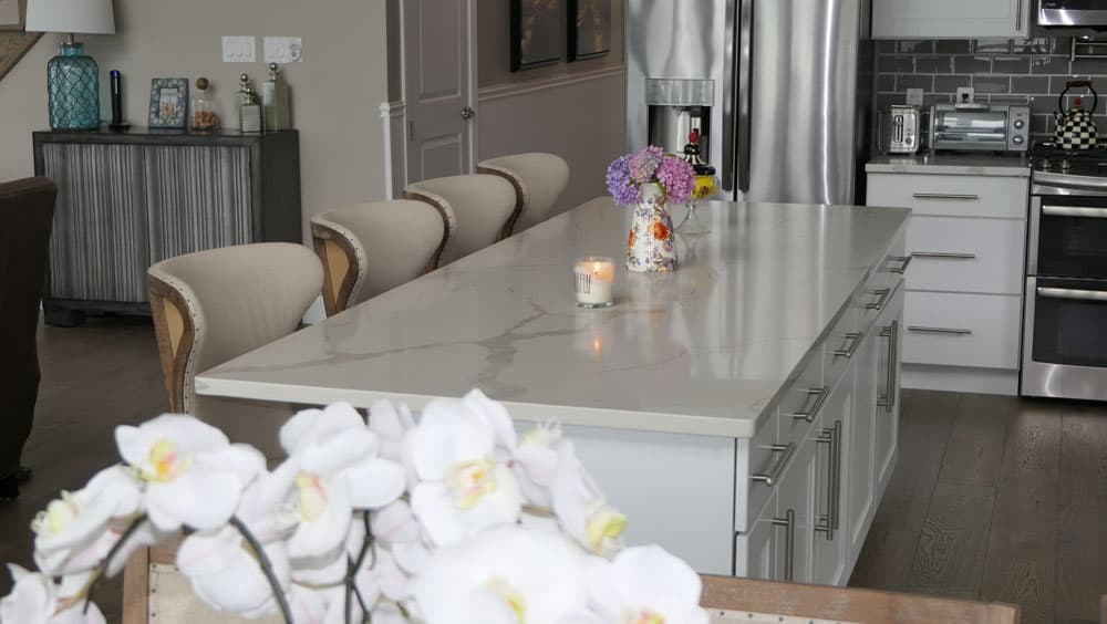 Kitchen island with white marble countertop, gray cabinetry, and upholstered dining chairs