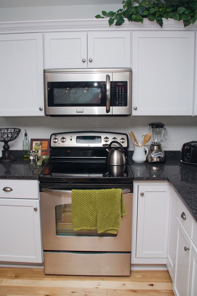 White kitchen with stainless steel range, over-the-range microwave, and dark granite countertops
