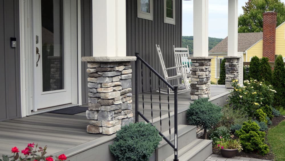 Front porch with stacked stone columns, metal railing, and white rocking chair