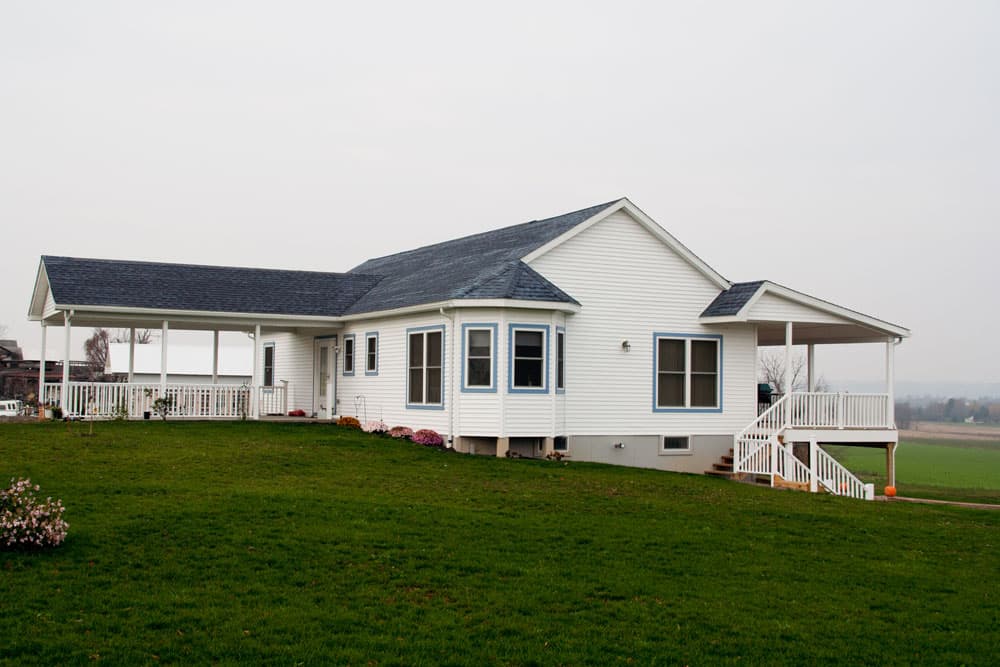 White modular home with dark roof, covered porches, and white railings on green lawn