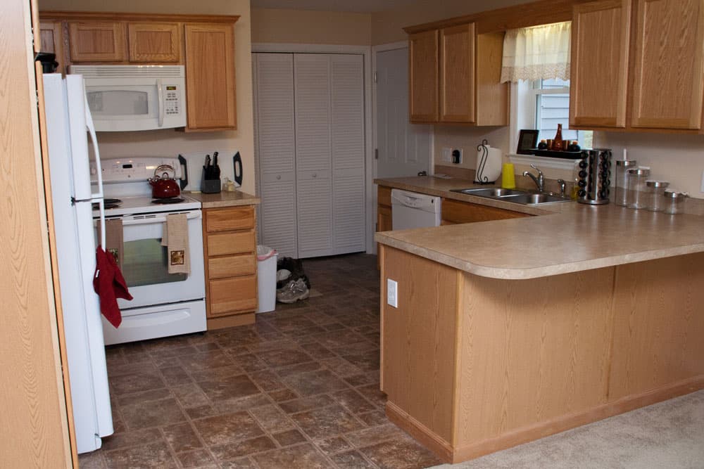Kitchen with oak cabinets, white appliances, beige countertops, and tile flooring