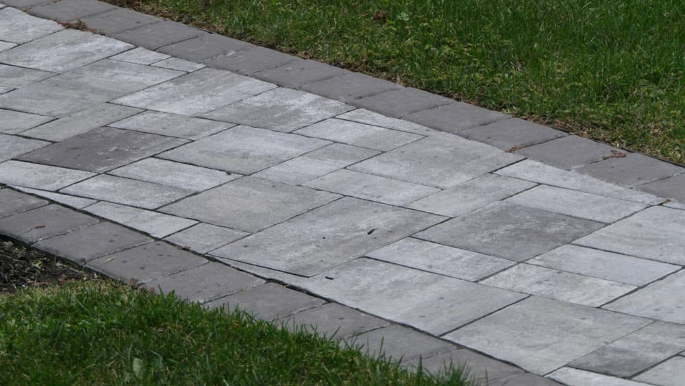 Gray paver stone walkway with herringbone pattern bordered by green lawn