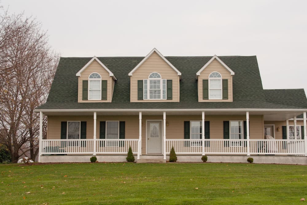 Tan cape cod style modular home with dark green shutters and full front porch