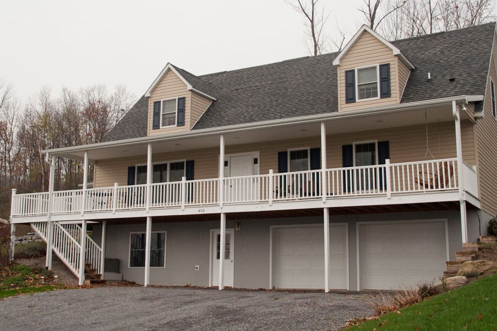 Two-story modular home with tan siding, dark shutters, and white wraparound porch