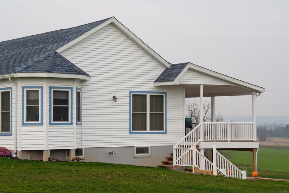 White vinyl-sided farmhouse with new covered deck addition and stairs overlooking rural farmland