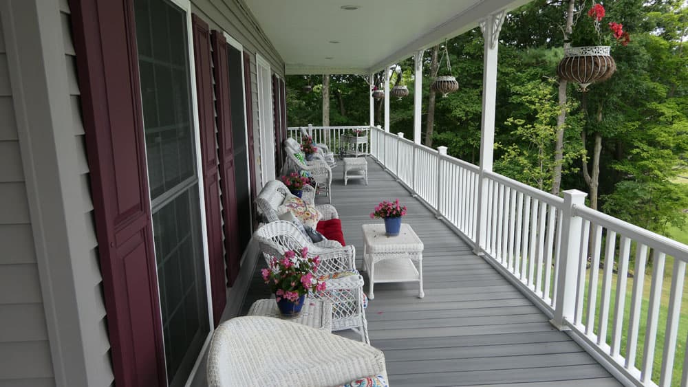 Long wraparound porch with white railings, wicker furniture, and hanging flower baskets
